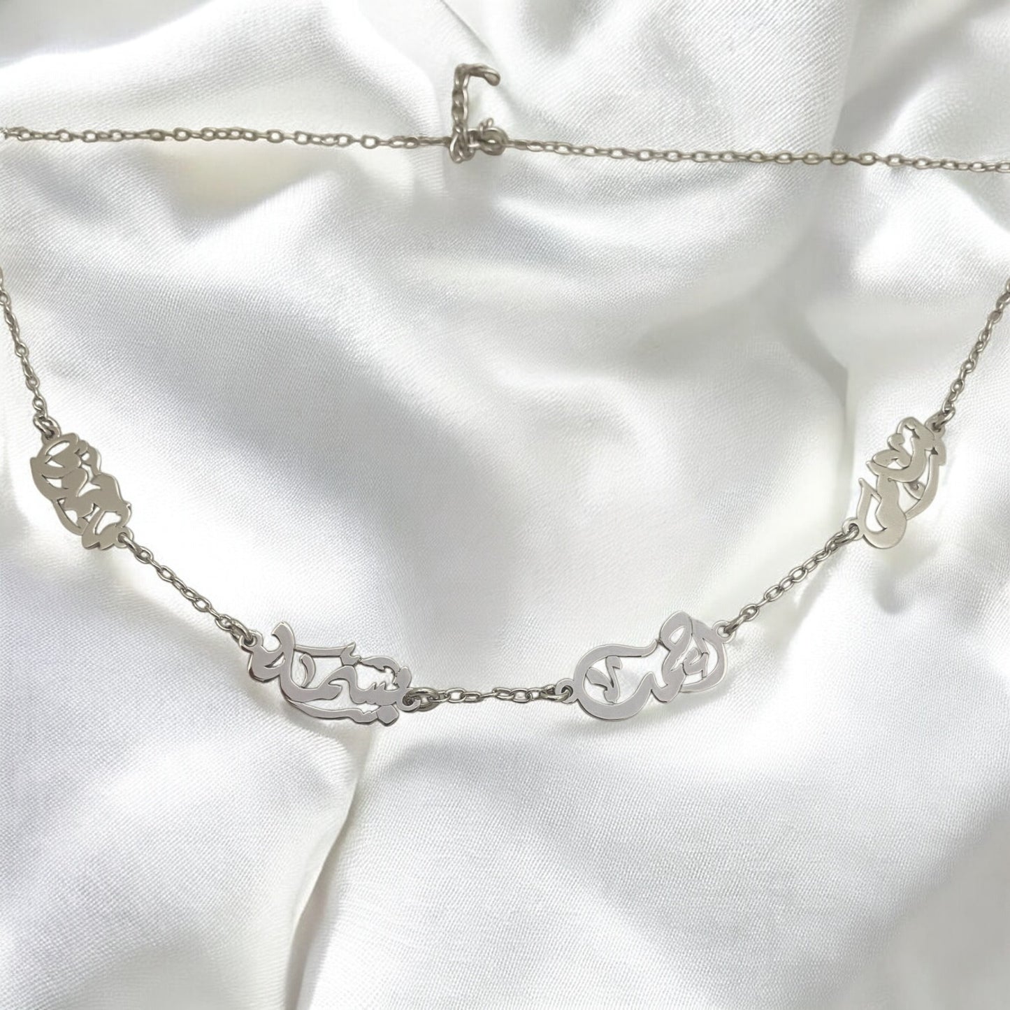 Silver necklace with intricate designs on a white fabric background